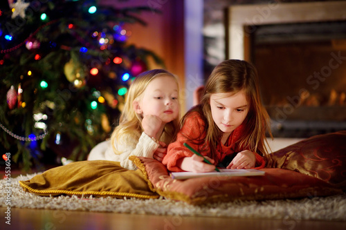 Two cute little sisters writing a letter to Santa by a fireplace on Christmas