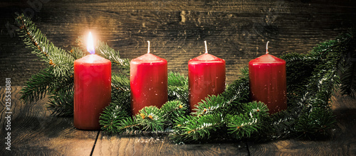Ersterer Advent: eine leuchtende Kerze vor einem Holzhintergund photo