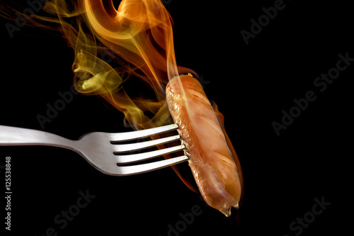Spicy sausage on black background with flame