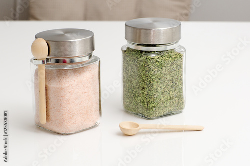 Pink salt and herbs are in the glass jars with spoons. Spice for cooking food on a white background. 
