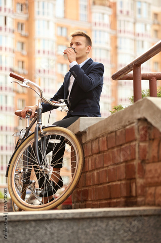 Coffee-to-go concept. Young man with bicycle and cup of coffee on street © Africa Studio