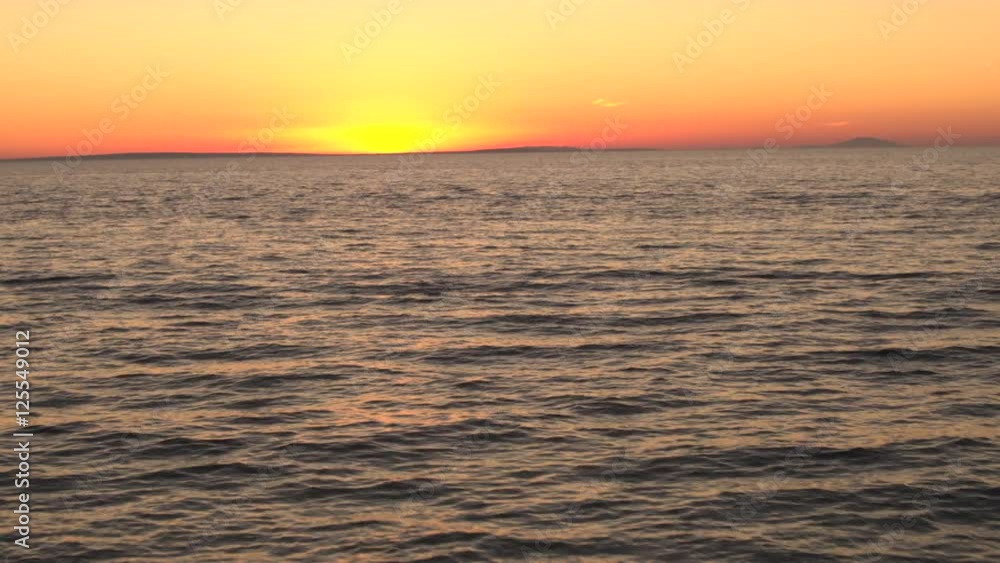 AERIAL: Girl in white dress looking at rippling sea and making heart shaped sign