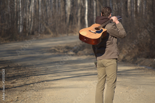 The man with the guitar standing on the road near forest