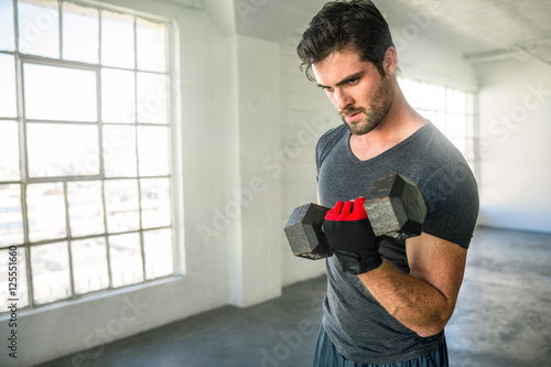 Foto Handsome athletic lean man lifting dumbbell in gym with large windows