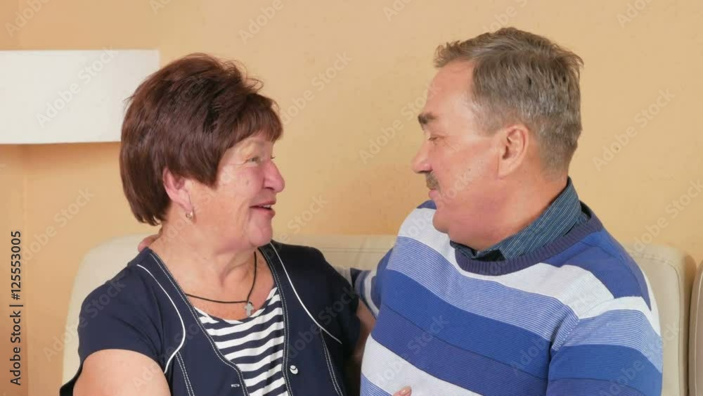 Happy elderly man returns home and embraces his beloved wife on a sofa in a beautiful house. They kiss, talk and laugh. Happy elderly man returns home and embraces his beloved wife on a sofa in a beautiful house. They kiss, talk and laugh.