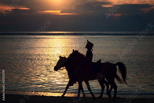 Rider with two horses at sunset on the beach