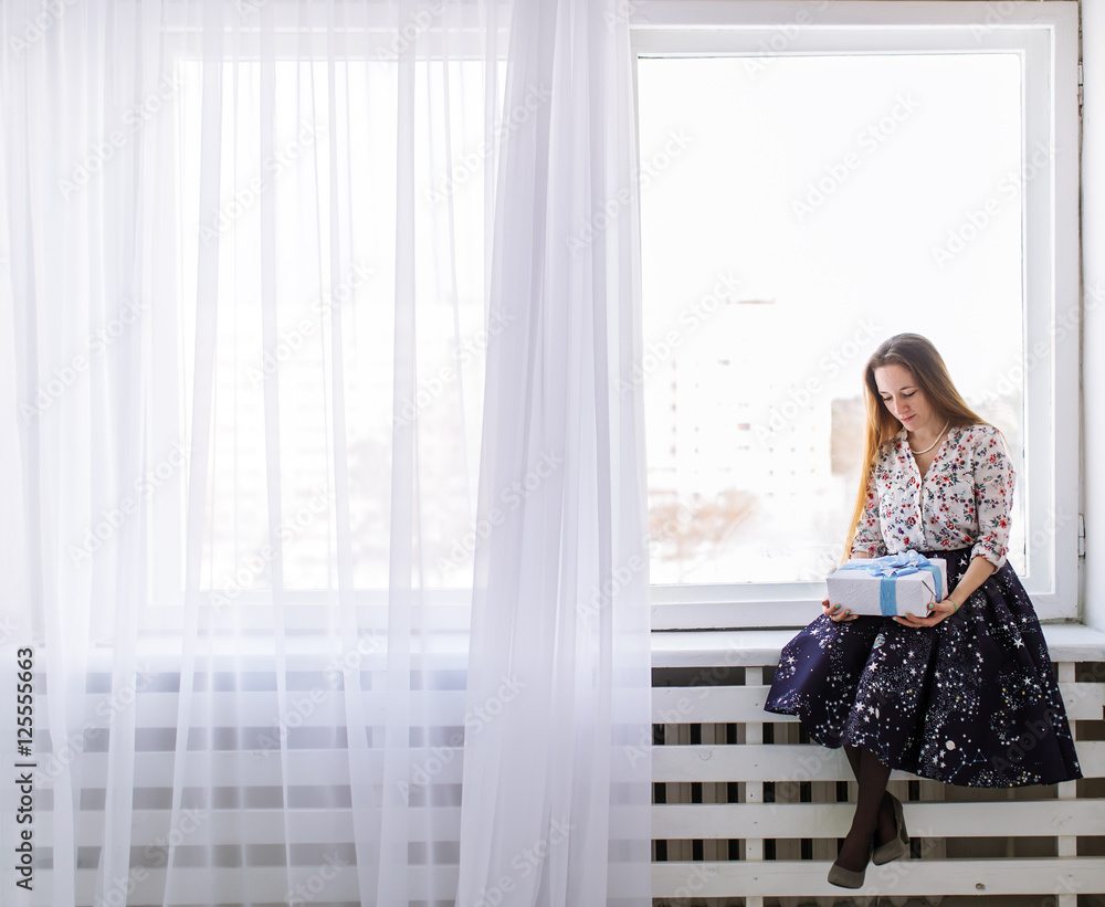The woman sits on window sill with a gift