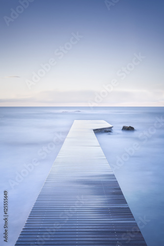 Wooden pier, rocks and calm sea on long exposure.