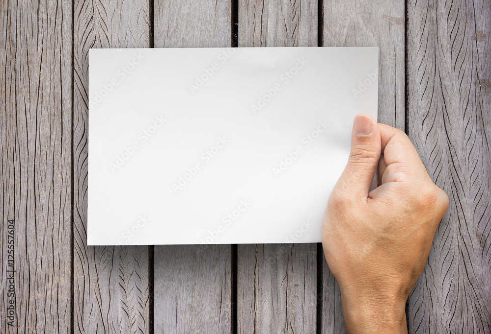 The hand holding a notes paper on wood background The hand holding a notes paper on wood background