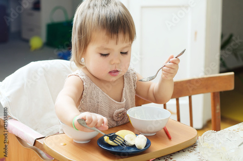 little girl eating in baby sitting, child using fork and spoon 