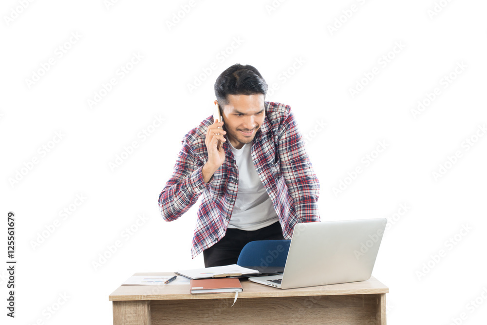 Young businessman talking on phone while working at laptop in of Young businessman talking on phone while working at laptop in of