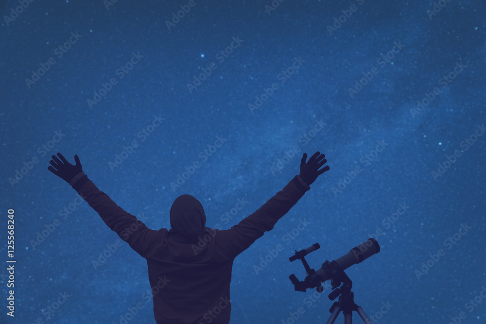 Man enjoying under the starry sky with telescope beside him.
