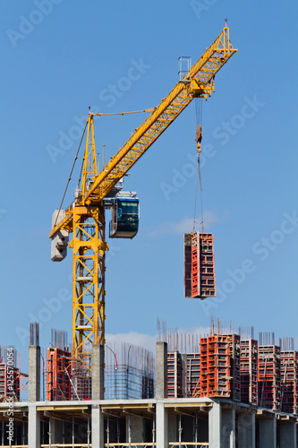 Yellow construction tower crane and house under construction