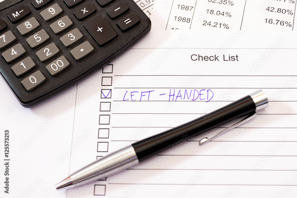 Left-handed ticked position on a check list with pen, calculator Left-handed ticked position on a check list with pen, calculator