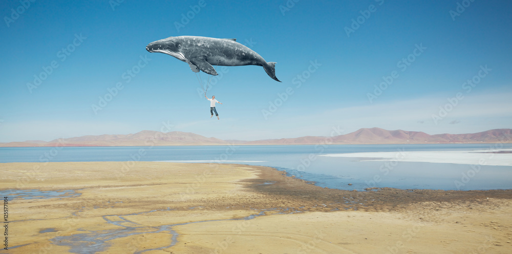 Naklejka premium Travel concept. Whale floats in the sky and carrying a happy young asian guy .