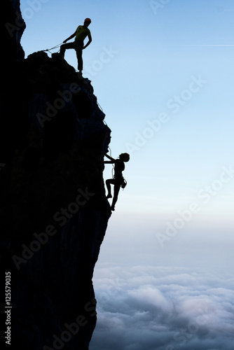 Teamwork couple  climbers in the wall. The first makes safety the second creating a perfect team. Team of climbers climbing helping each other on top of mountain, climbing trust beautiful landscape. photo