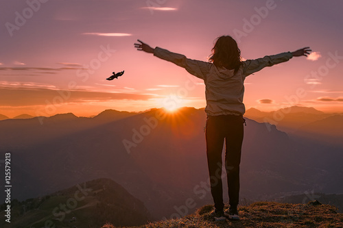 Woman on top of a mountain at sunset looks eagle