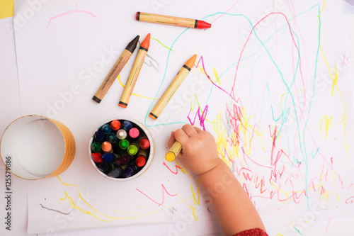 A hand of baby drawing on the white paper with colorful crayons.