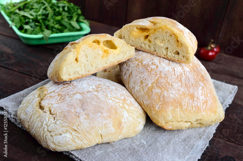 Ciabatta with cheese stuffing - freshly baked Italian white bread on a dark wooden background. For the preparation of sandwiches.