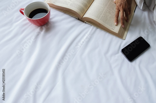 Beautiful asian female sitting on the bed with a cup of coffee and reading a book. Morning with a book and cup of coffee. Relaxing concept. Retro filter effect soft focus selective focus.