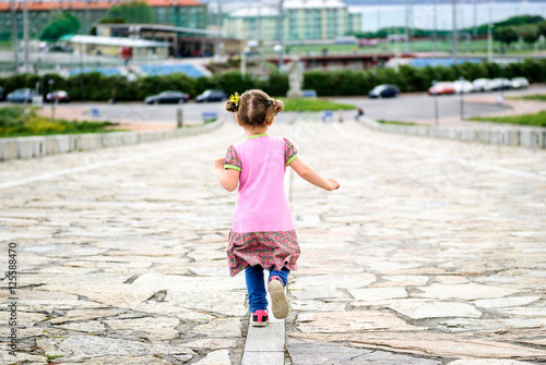 Little girl is running on stone paved promenade at Hercules Tower, a Coruna - Spain. © _jure
