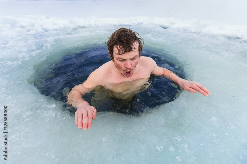 Young man swimming in the winter lake in the ice hole