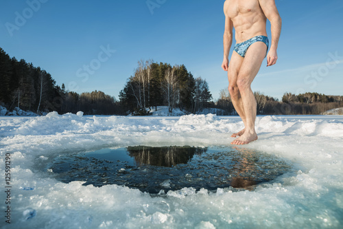 Young man going to swim in the winter lake in the ice hole