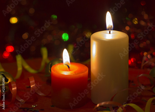 Christmas and New Year`s festive evening burning candle bokeh image. Greeting card lights Background concept with holiday tinsel, twisted ribbons and copyspace place for text or logo.
