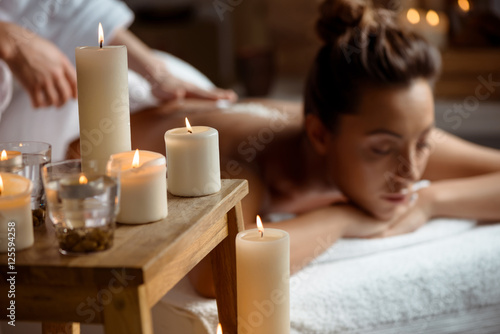Young beautiful girl relaxing in spa salon. Focus on candles.