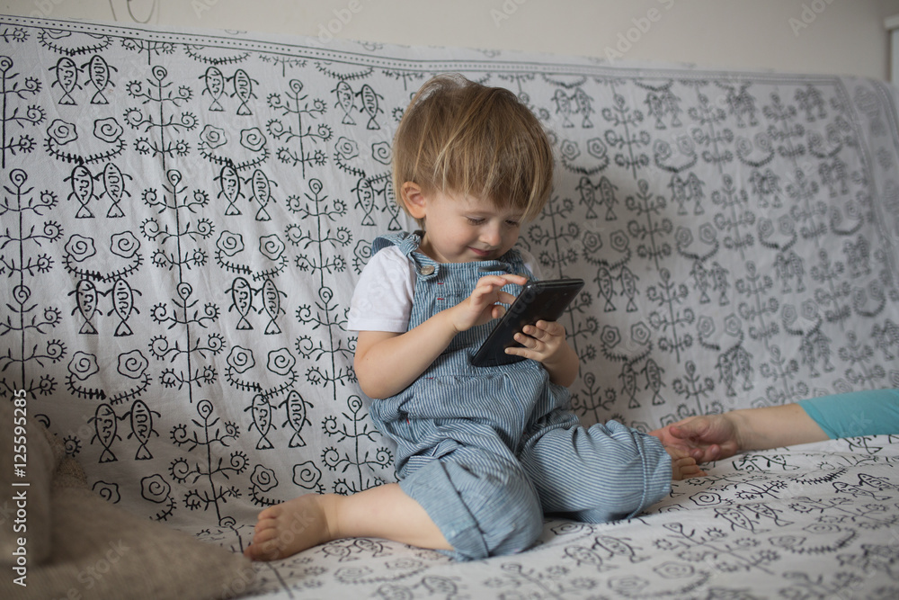 Naklejka premium Toddler boy playing with phone, in light room lifestyle, real in