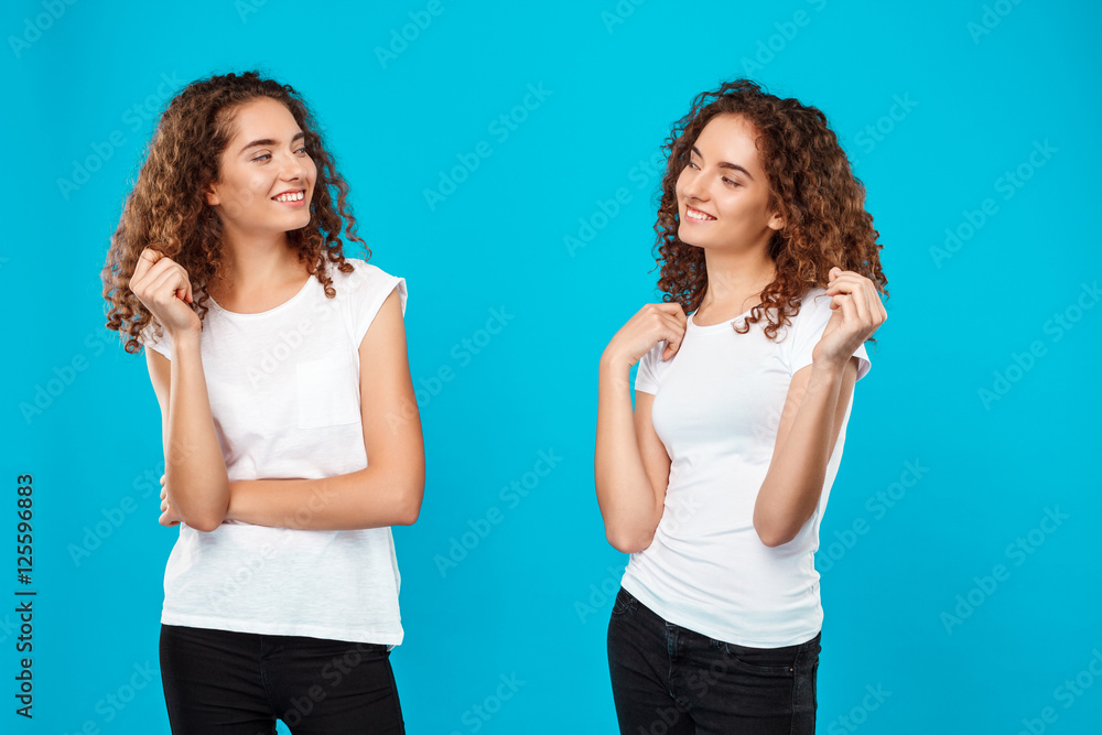 Two girls twins looking at each other over blue background. Two girls twins looking at each other over blue background.