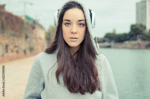 Half length of young beautiful brunette straight hair woman in the city with headphones listening to music, looking in camera photo