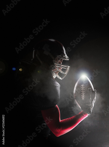 American football player posing with ball on black background © master1305