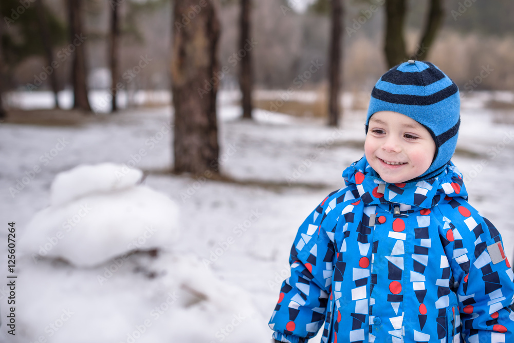 Winter portrait of kid boy in colorful clothes, outdoors during snowfall. Active outoors leisure with children in  on cold snowy days. Happy toddler child having fun  snow in forest.
