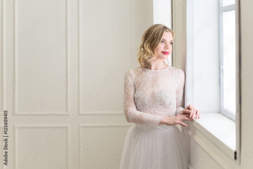 Beautiful bride standing at window in white room. Beautiful bride standing at window in white room.