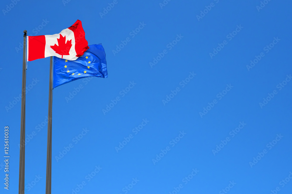 Canadian and European flags waving in the wind over blue sky