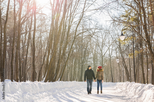 Couple holding each other's hands, the winter goes on the road, enjoying a stroll, a love couple. Husband and wife are going through the park holding hands in the winter. The movement of people