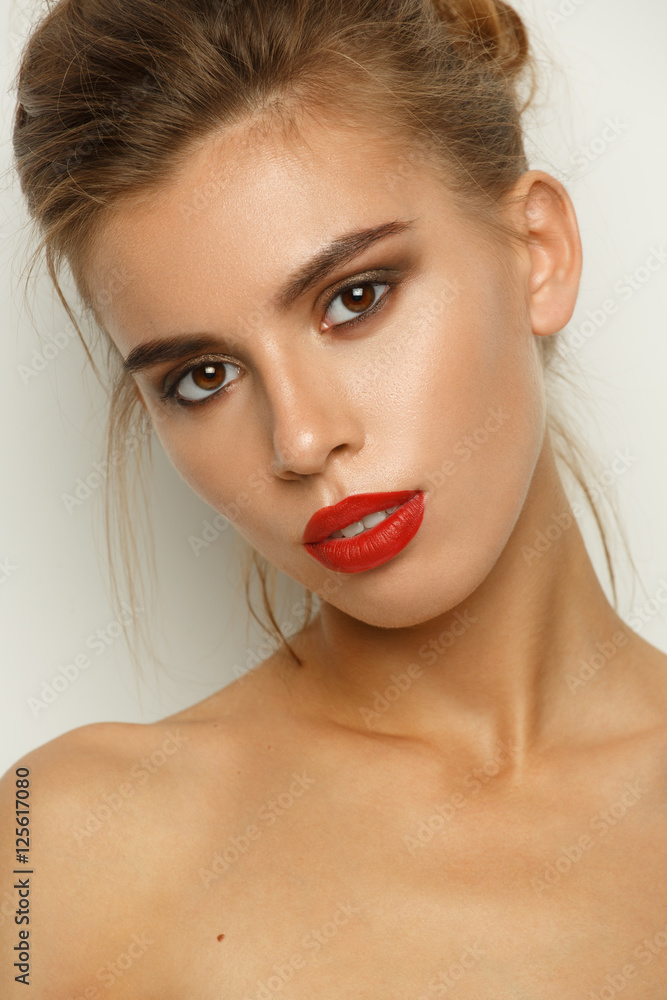 Fashionable contrasty portrait of a sexy beautiful young woman with perfect makeup (smooth glowing skin, wide groomed eyebrows, red lipstick and smokey eyes), studio shoot, light background Fashionable contrasty portrait of a sexy beautiful young woman with perfect makeup (smooth glowing skin, wide groomed eyebrows, red lipstick and smokey eyes), studio shoot, light background