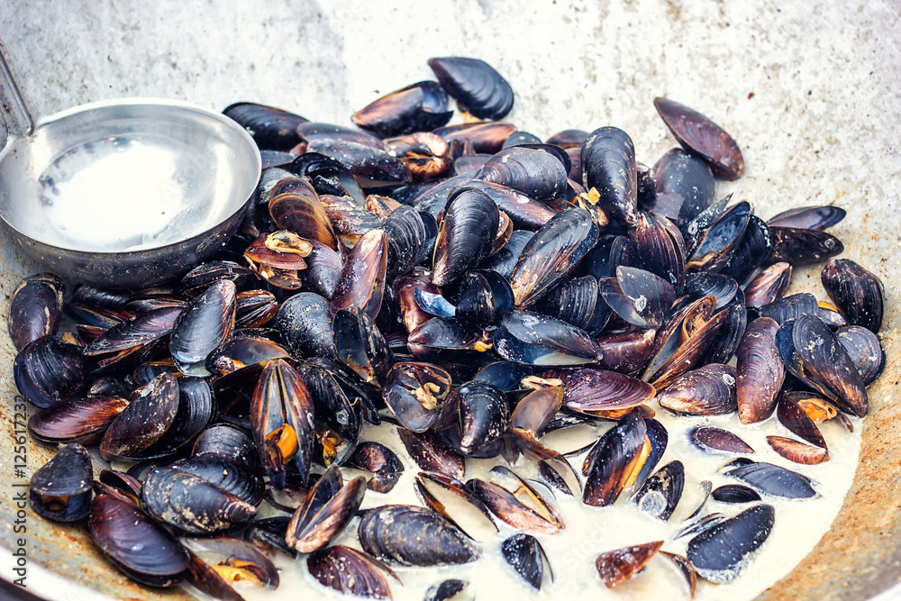 Steamed mussels in white wine sauce cooking at large metallic pan. Fresh mussels at grill pan. Seafood barbecue outdoors. Picnic healthy food, mussels in shells. Stewed clams, mediterranean cuisine. Steamed mussels in white wine sauce cooking at large metallic pan. Fresh mussels at grill pan. Seafood barbecue outdoors. Picnic healthy food, mussels in shells. Stewed clams, mediterranean cuisine.
