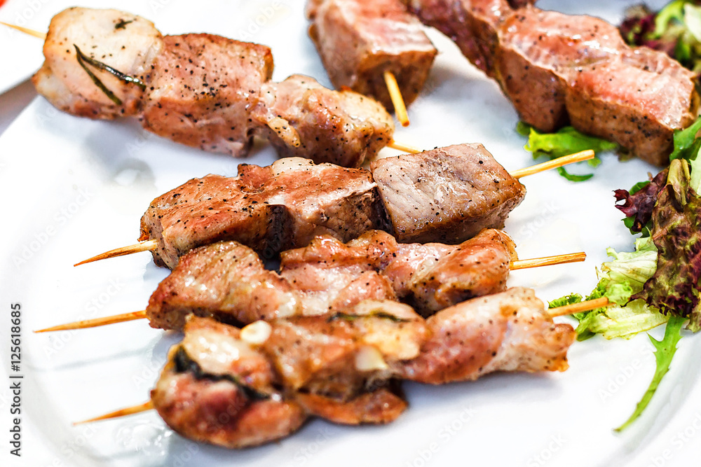 Grilled meat kebabs on the white plate. Skewered on wooden sticks tasty pork meat. Shashlik or Shish kabab.
