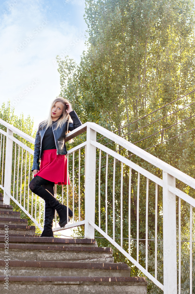 A blonde woman in a red skirt and a black jacket on the stairs
