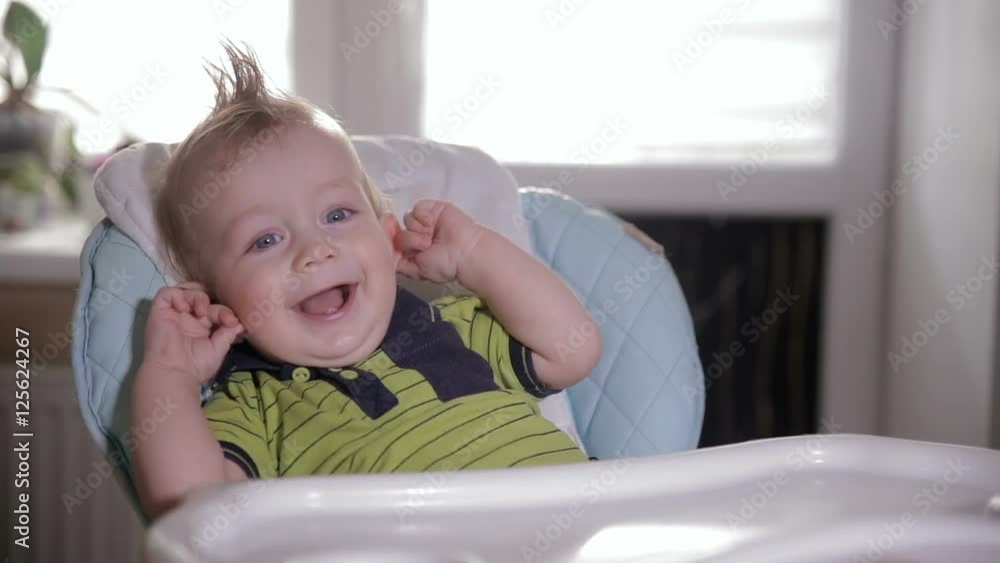 Cute shy baby in a baby chair laughing and looking into camera. HD. Cute shy baby in a baby chair laughing and looking into camera. HD.