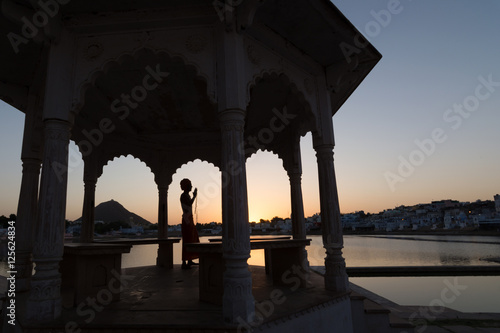 Tableau sur toile Silhouette of a sadhu performing ritual prayer in the evening at Pushkar Lake