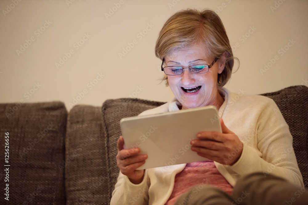 Senior woman with tablet sitting on couch in living room Senior woman with tablet sitting on couch in living room