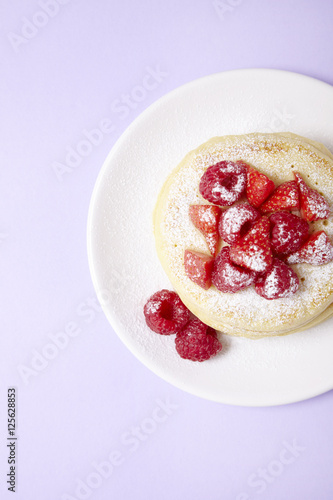 Aerial view of a stack of fruit covered pancakes on a pastel purple background