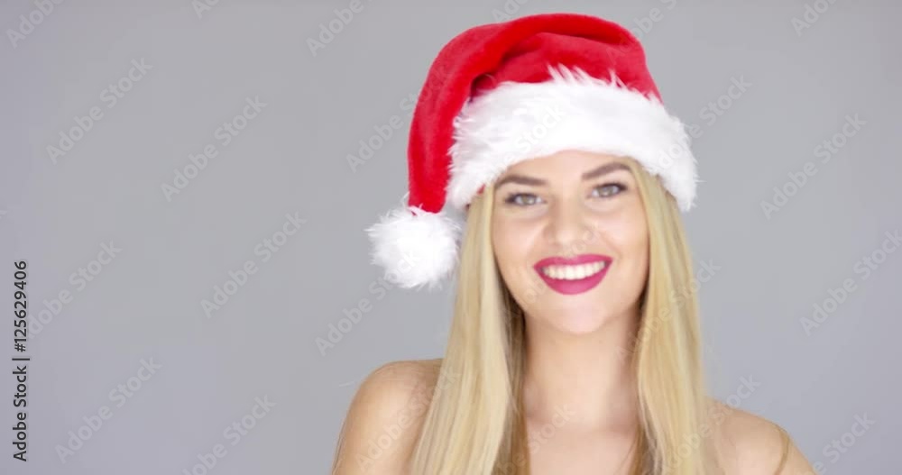 Pretty young woman posing in Santa Claus Hat. She is isolated on gray background. Sending warm kiss to the camera and smile Pretty young woman posing in Santa Claus Hat. She is isolated on gray background. Sending warm kiss to the camera and smile