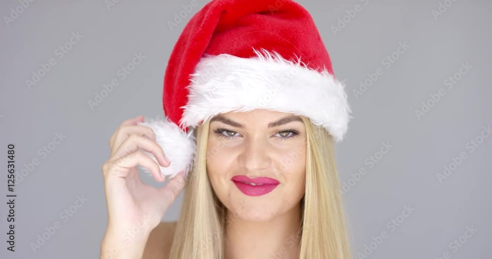 Beautiful chick in Santa Claus Hat posing with sensual smile while isolated on gray background. She has long blond hair and bare shoulders. Beautiful chick in Santa Claus Hat posing with sensual smile while isolated on gray background. She has long blond hair and bare shoulders.