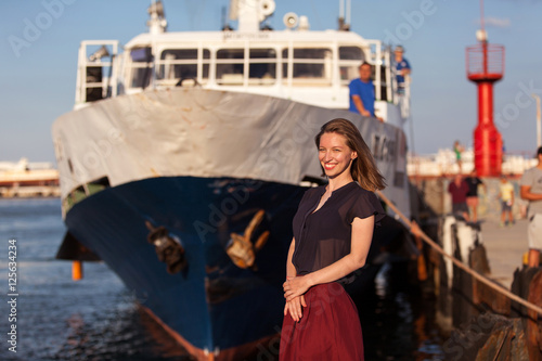 Smiling woman in front of a ship in a harbor