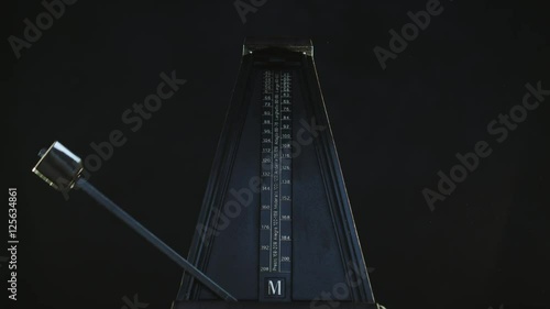 Close-up shot of vintage metronome with golden pendulum beats slow rhythm on the dark background