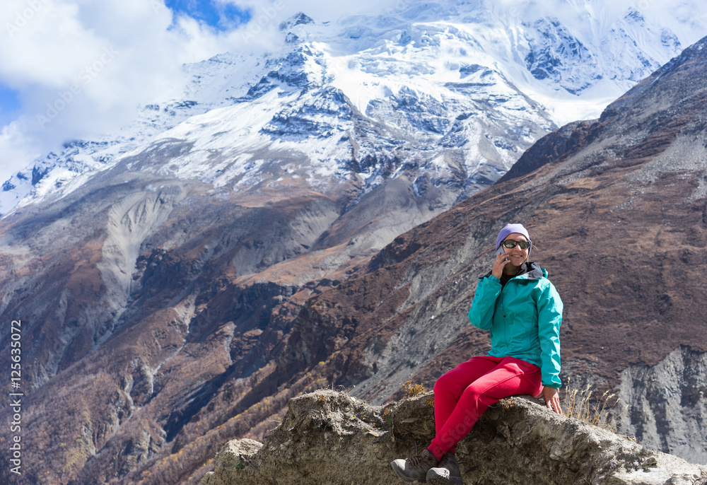 Fototapeta premium Hiker sitting, talking on mobile and enjoying a view on beautiful mountains from top of mountain. Himalayas, Nepal.
